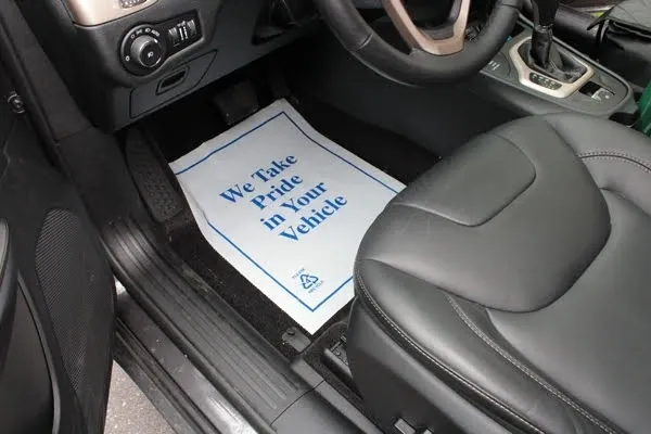 Paper floor mat on the driver's side of a vehicle's interior with the text "we take pride in your vehicle" on it.